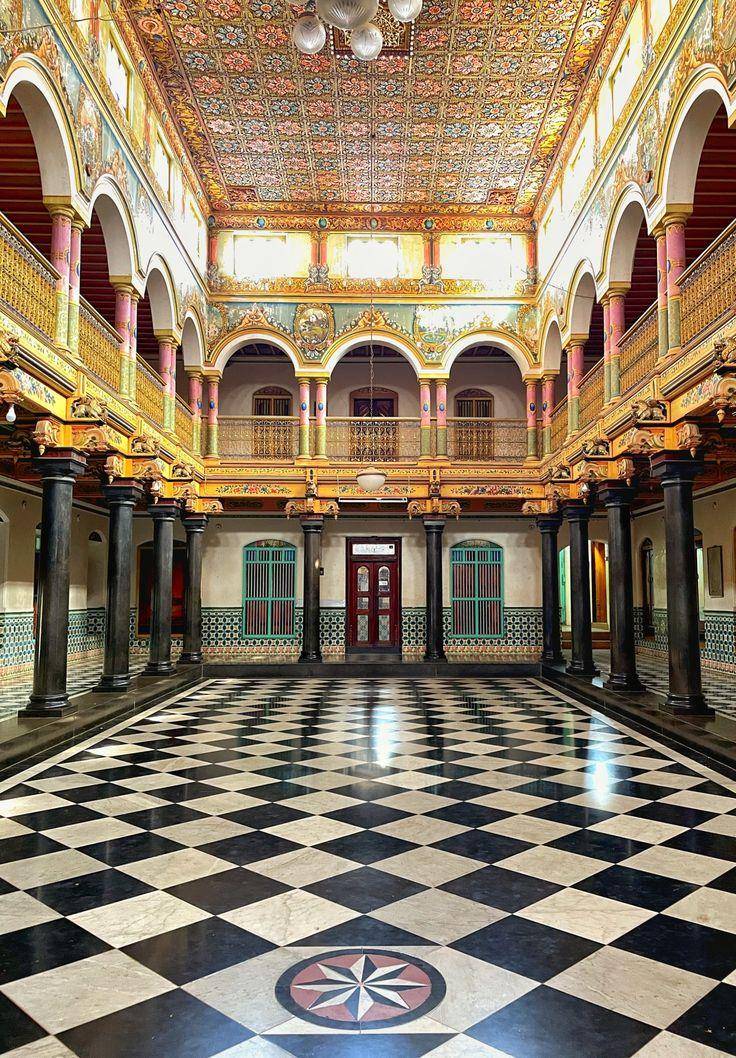 Ornate hall of a Chettinad mansion with painted ceiling and black-and-white floor